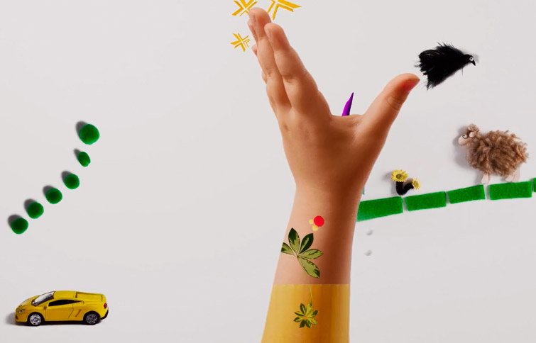 Das Bild zeigt eine kleine Kinderhand, die sich neugierig in die Luft streckt. Um die Hand fliegen Elemente aus den DBSV-Tastbüchern, wie zum Beispiel ein keines Schaf und ein gelbes Spielauto.