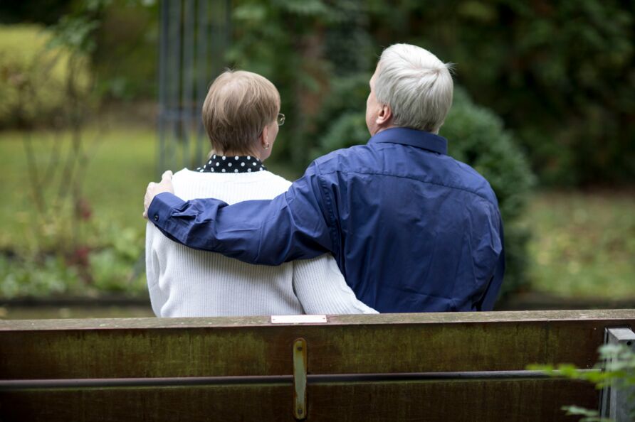 Ein Mann und eine Frau sitzen auf einer Bank. Der Mann hat den Arm um die Frau gelegt.