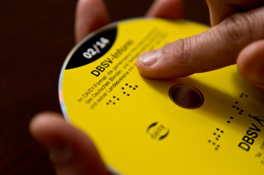 Jemand liest mit dem Finger die Brailleprägung auf der DBSV-Inform DAISY-CD